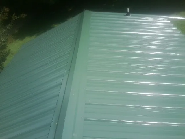 New green metal panels meeting at the ridge of a roof — Flat Roof Repair work by our crew in Redmond