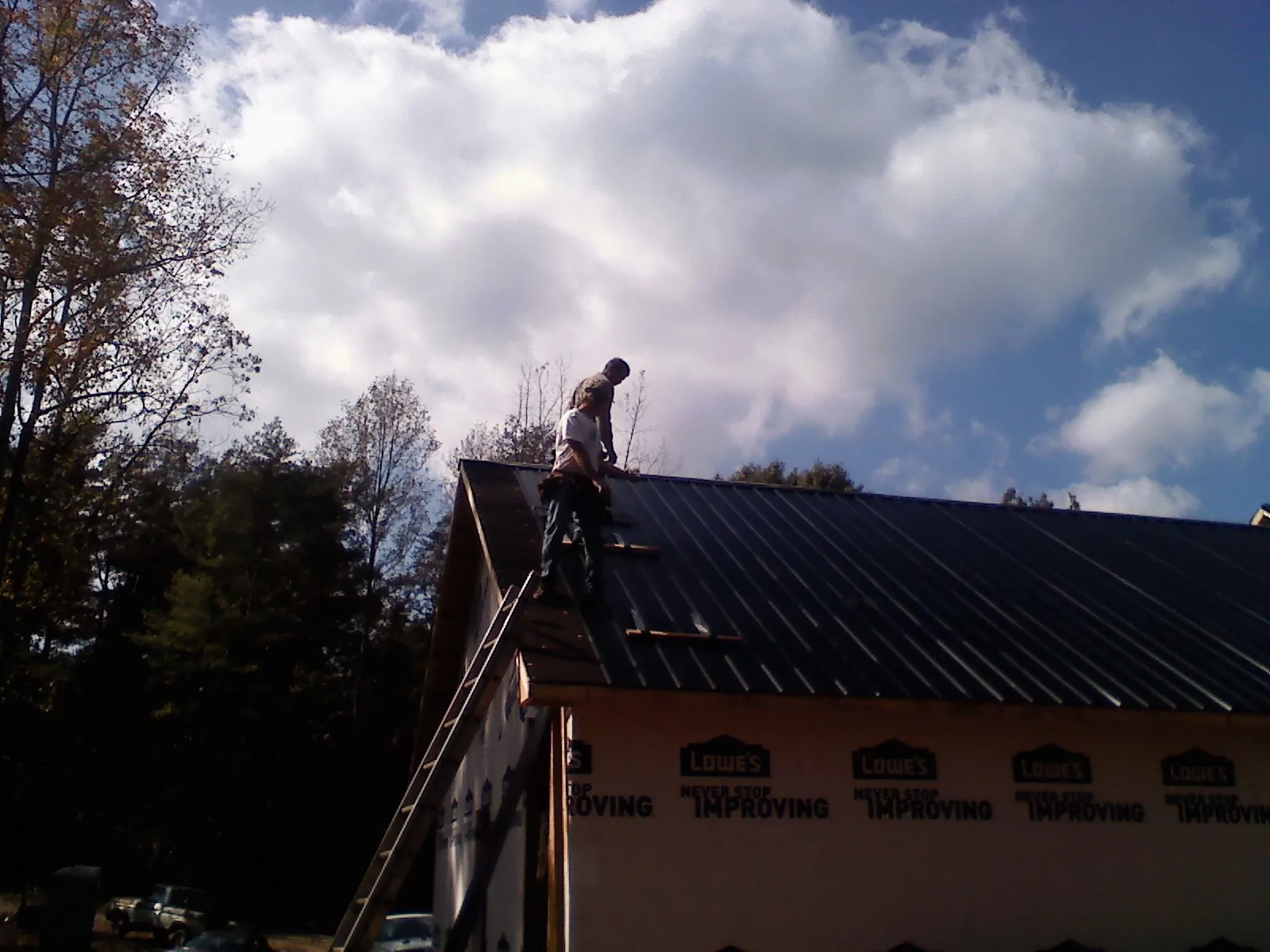 Roofer fastening dark metal panels high against a cloudy sky, from a Roof Inspection job in Redmond