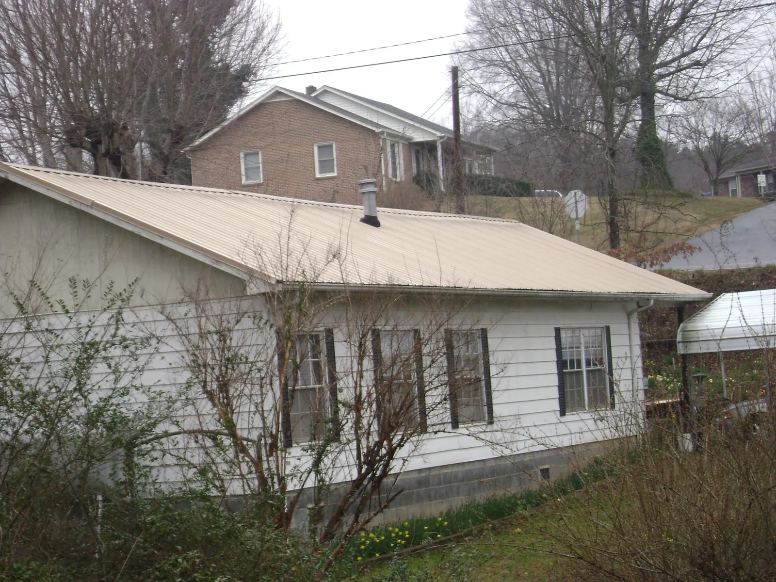 Tan metal roof on a white sided house set into a hillside — Commercial Roofing by Roofing Brothers in Redmond